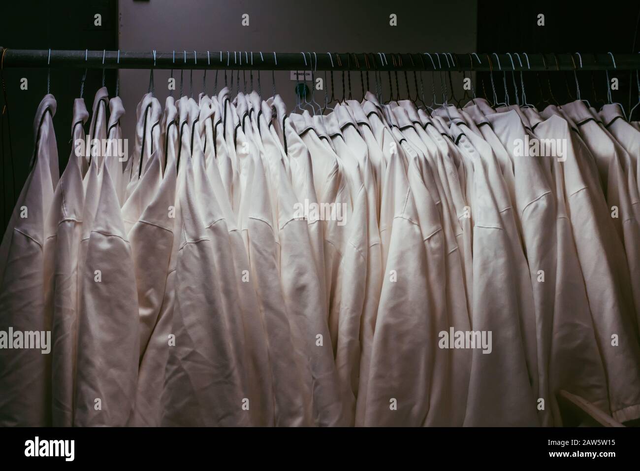 L'uniforme bianca è appesa in un armadietto scuro. Le giacche mediche sono pronte per l'uso. Abbigliamento tessile speciale per un uso diverso. armadio dell'ospedale. Foto Stock