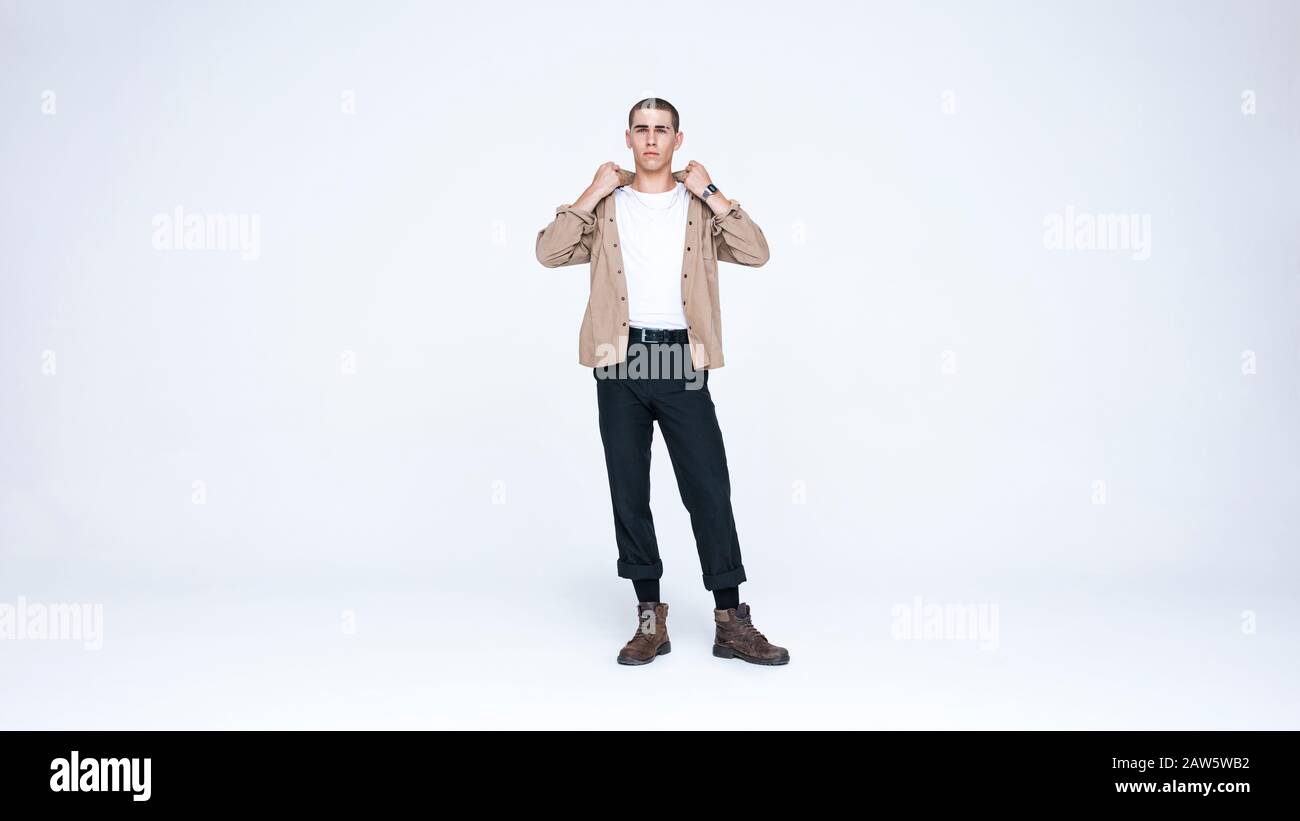 Giovane caucasico che guarda la fotocamera che tiene il collare della sua camicia. Uomo informale isolato su sfondo bianco. Foto Stock