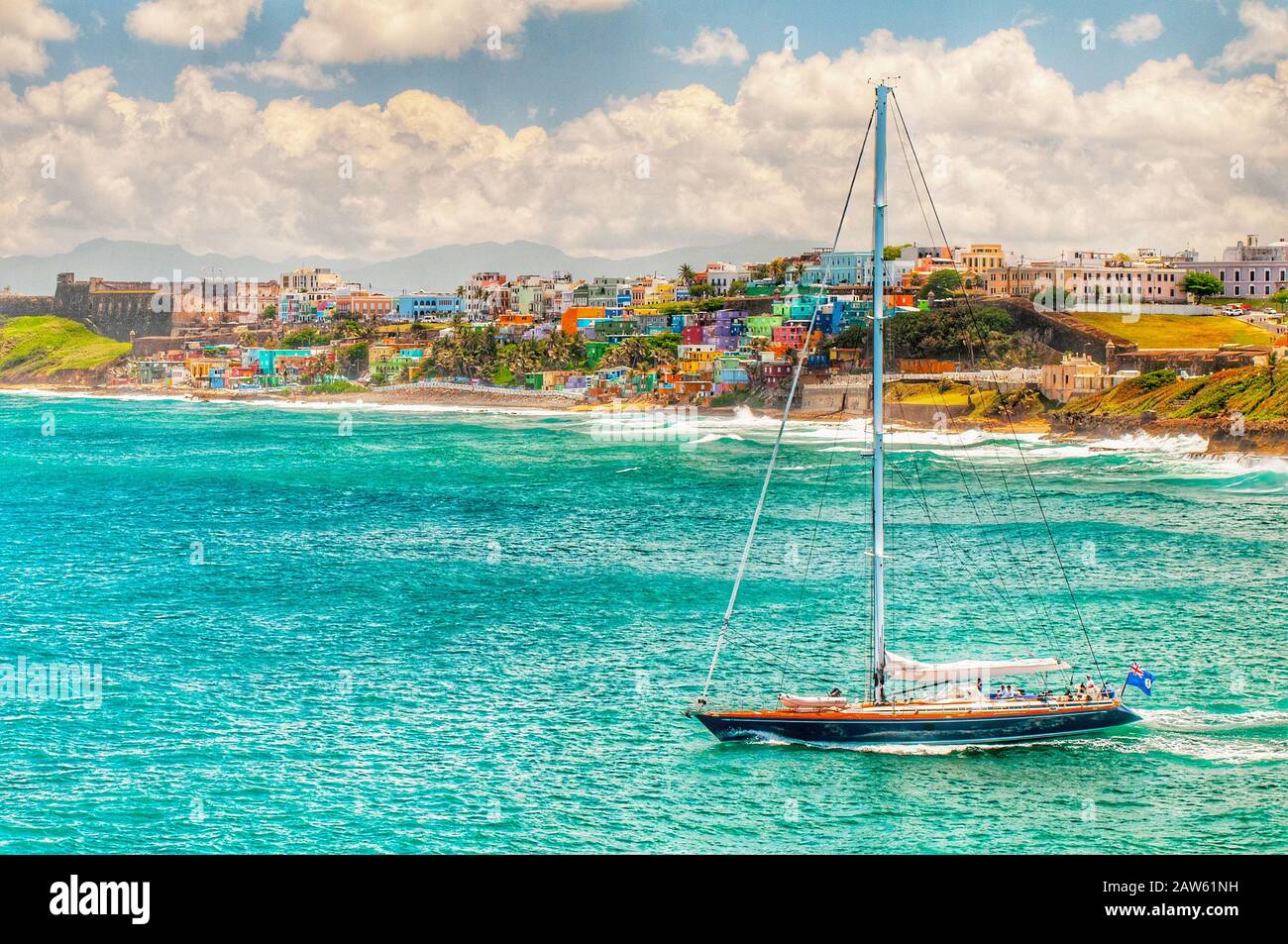 Case colorate fiancheggiano la collina che si affaccia sulla spiaggia e una barca a vela a San Juan, Puerto Rico Foto Stock