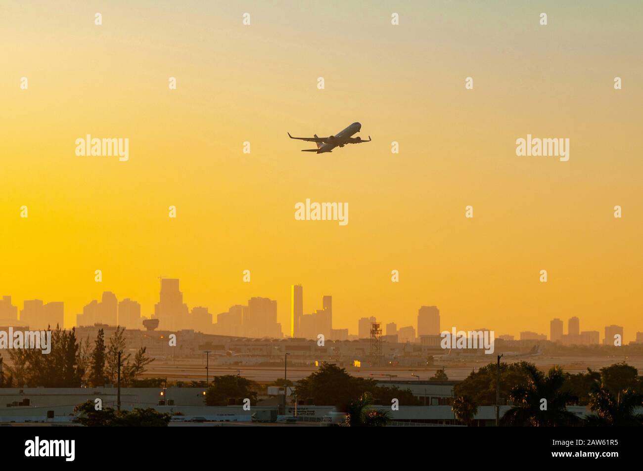 Un aereo si staglia contro un colorato alba giallo e arancione mentre parte dall'aeroporto di Miami con la città sullo sfondo. Foto Stock