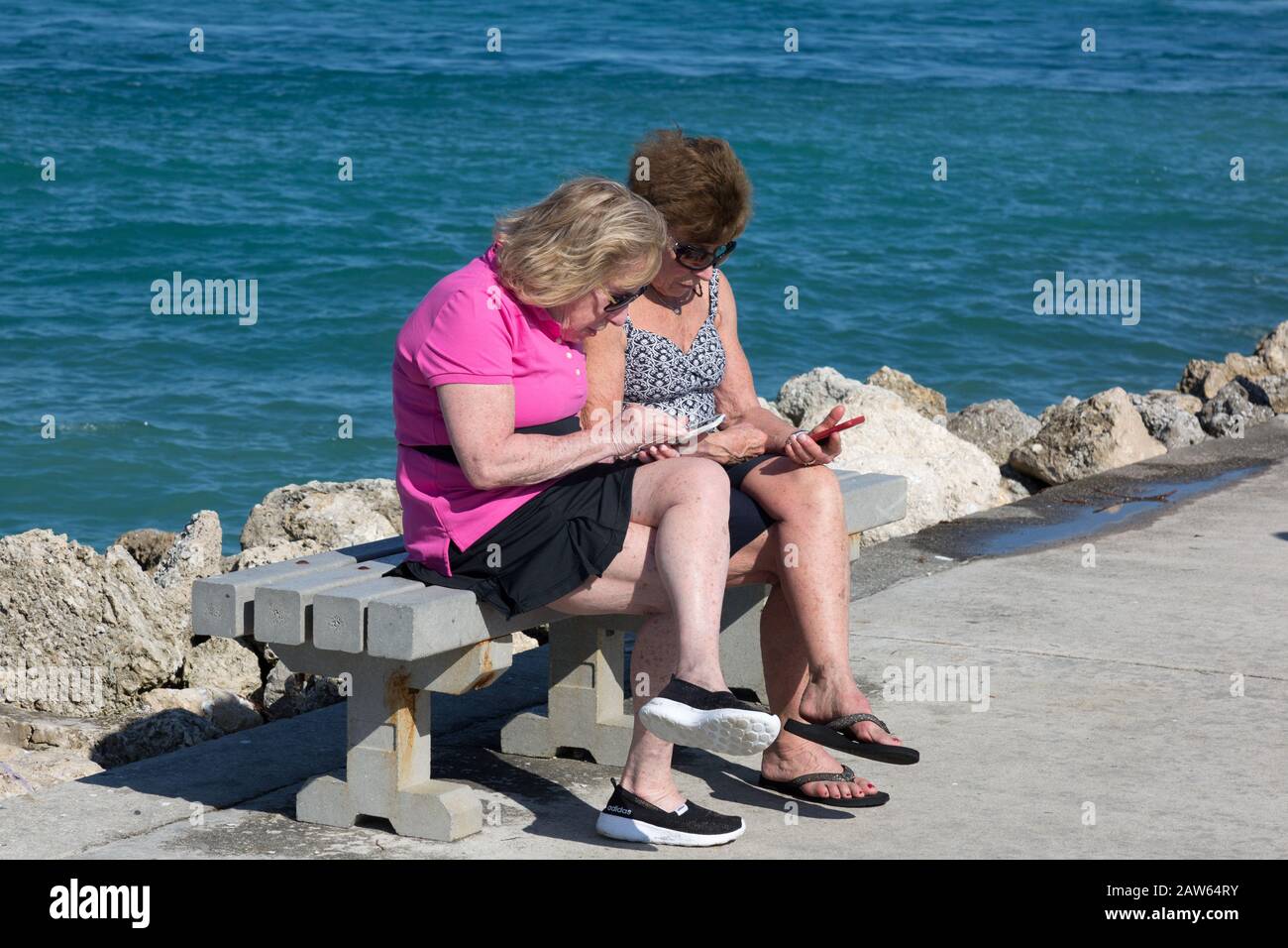 Due donne anziane tentano di usare i loro telefoni cellulari mentre si siedono su una panchina sul molo a Fort Pierce Inlet sulla Treasure Coast nella contea di St Lucie. Foto Stock