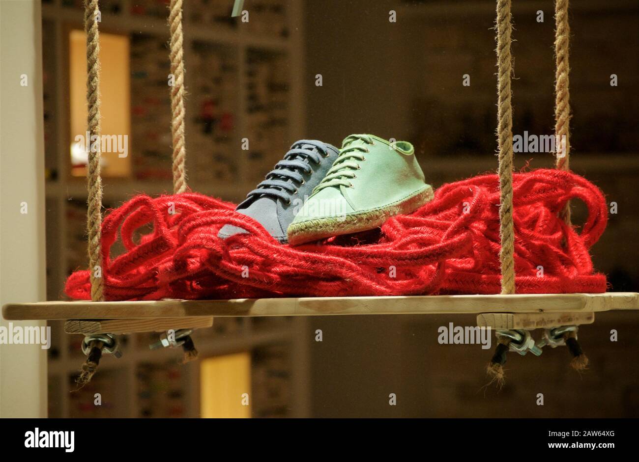 Un paio di scarpe espadrille uno blu l'altro verde chiaro su una corda rossa su un altalena Foto Stock
