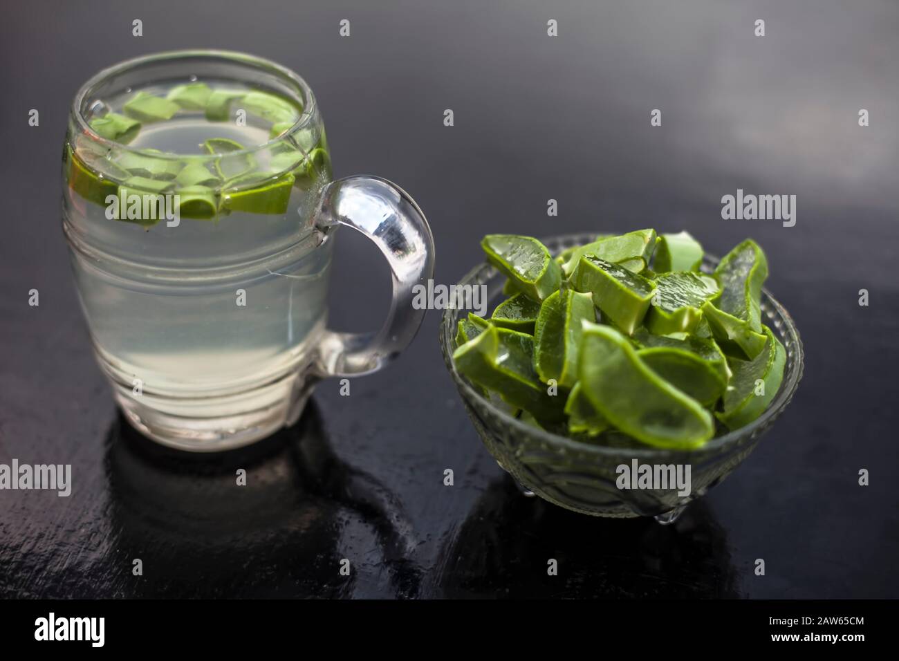 In prossimità della tazza di vetro su una superficie di legno contenenti aloe vera detox drink nel lungo con il suo intero ingredienti grezzi con esso. Inquadratura orizzontale con blurre Foto Stock