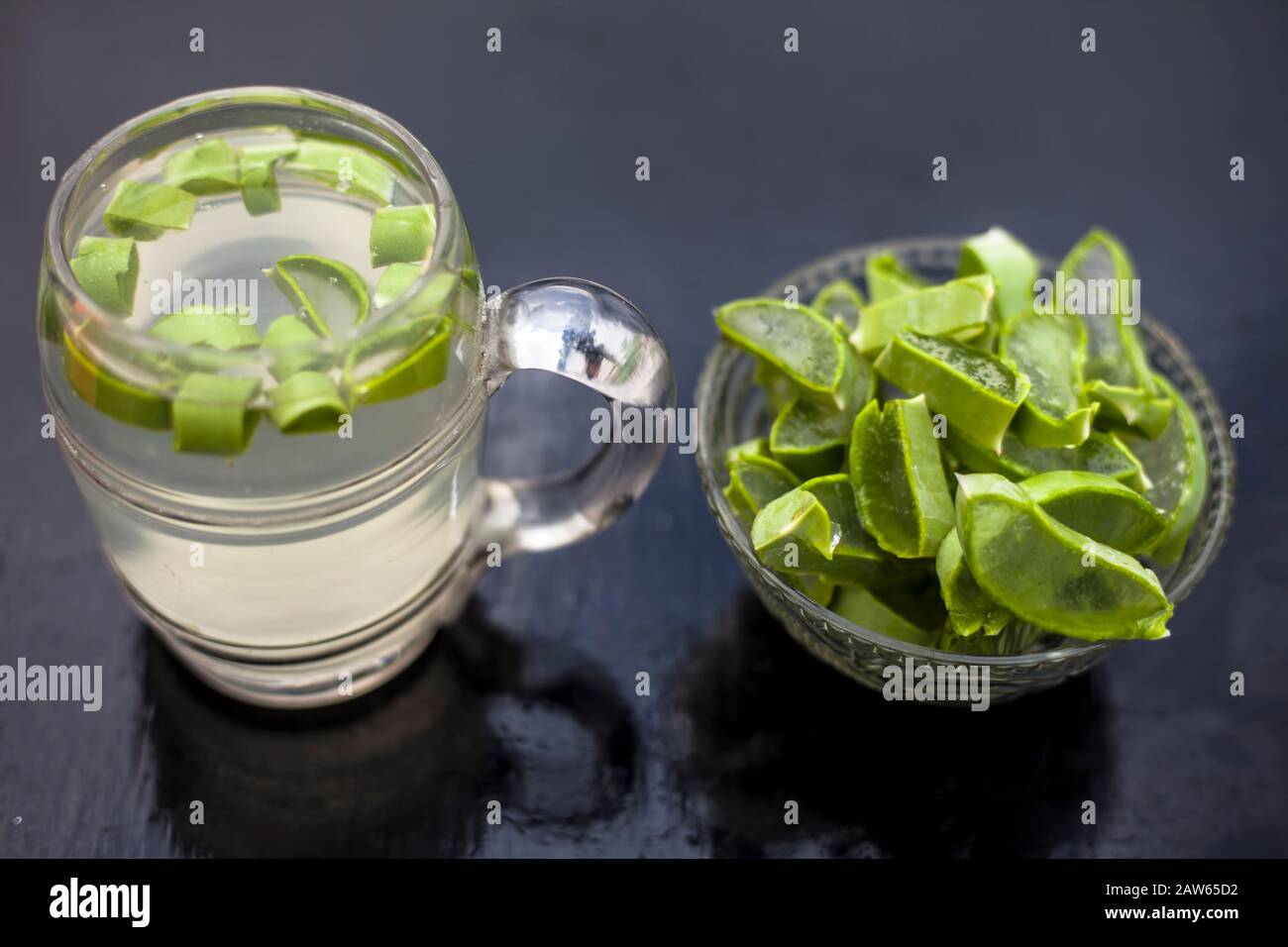 In prossimità della tazza di vetro su una superficie di legno contenenti aloe vera detox drink nel lungo con il suo intero ingredienti grezzi con esso. Inquadratura orizzontale con blurre Foto Stock