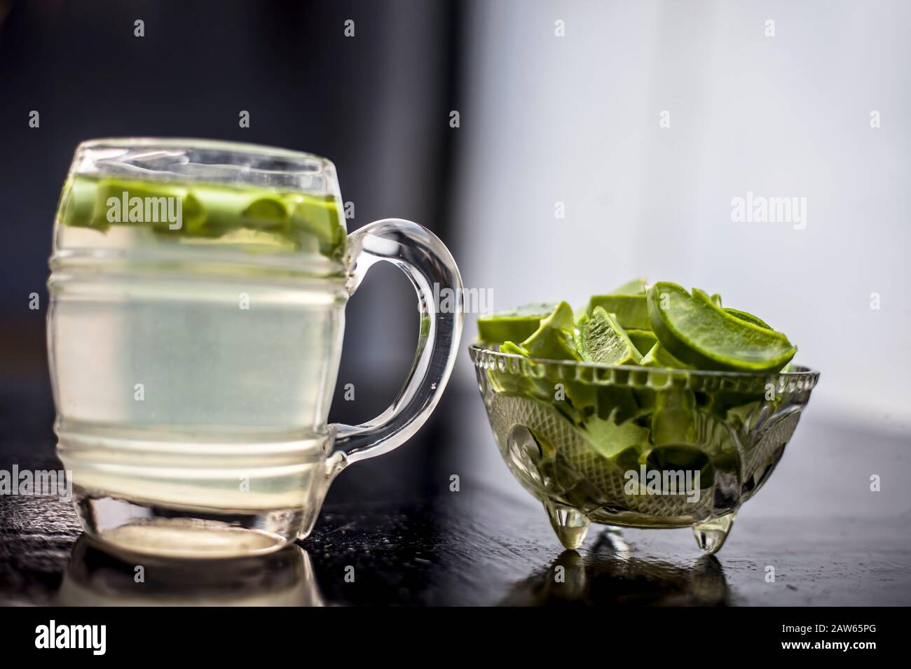 In prossimità della tazza di vetro su una superficie di legno contenenti aloe vera detox drink nel lungo con il suo intero ingredienti grezzi con esso. Inquadratura orizzontale con blurre Foto Stock