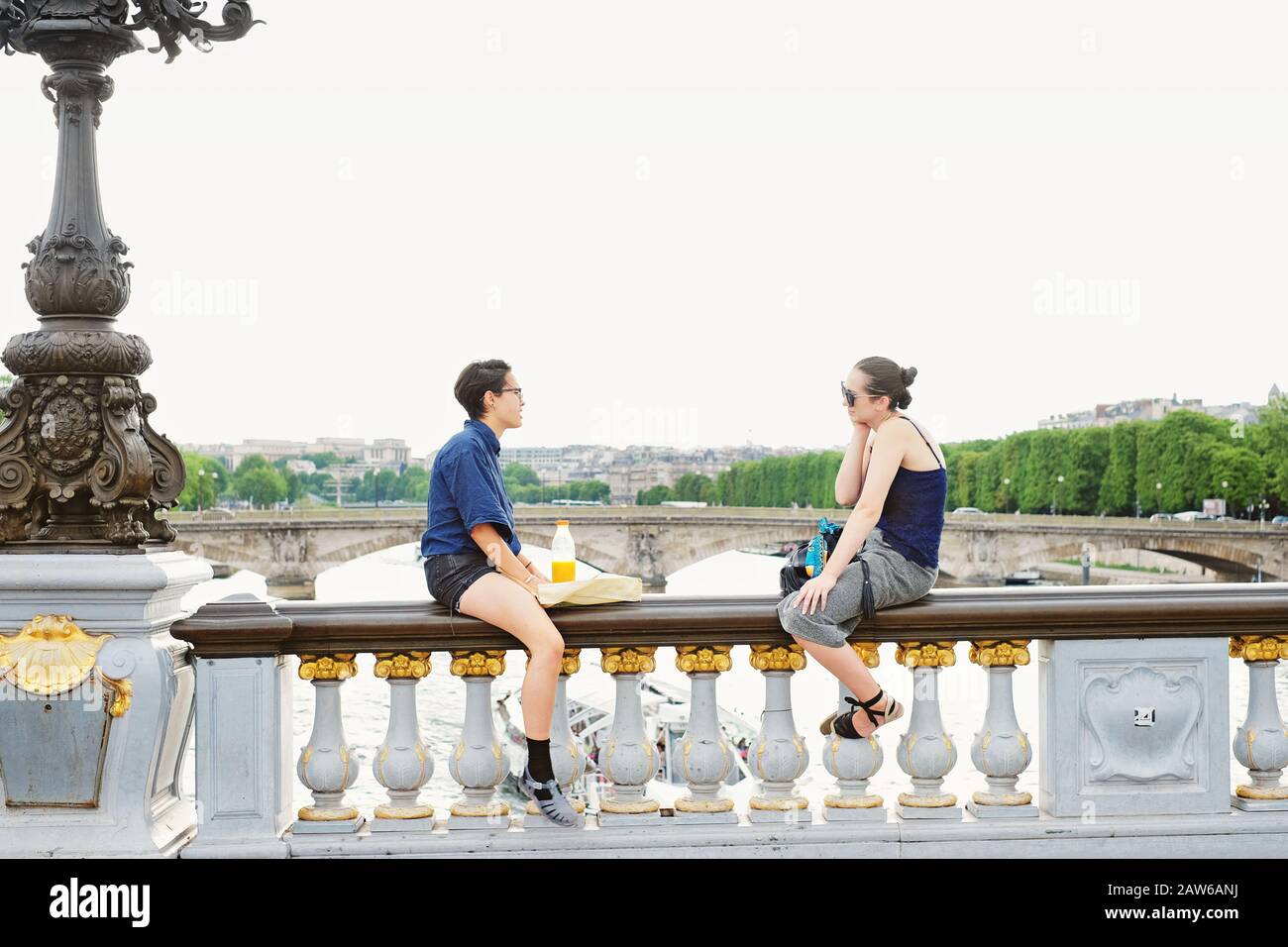 Due giovani donne si godono un pranzo al sacco e una conversazione sedute sull'ampia balaustra di bronzo del Pont Alexandre III; Pont des Invalides Paris, Francia Foto Stock