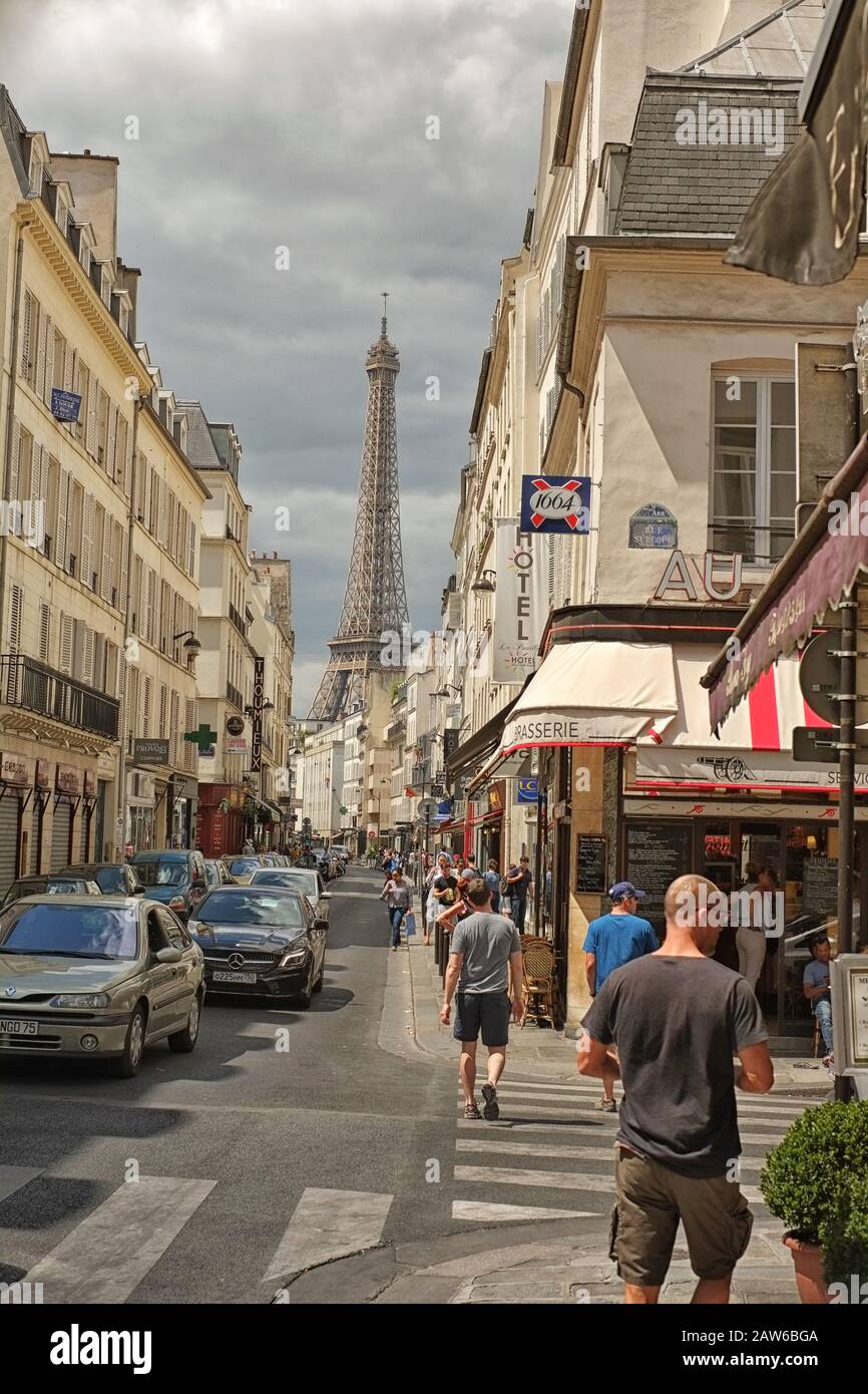 Una classica vista parigina della Torre Eiffel con persone che camminano in Rue Saint-Dominique, automobili, finestre, caffetterie e negozi, fiancheggiano il canyon della strada stretta Foto Stock