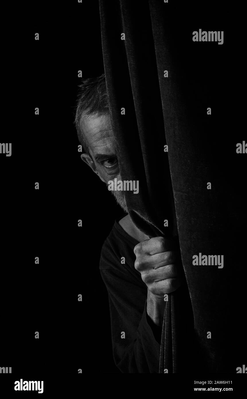 Un uomo spaventato si porca fuori da dietro un sipario in bianco e nero. Foto Stock