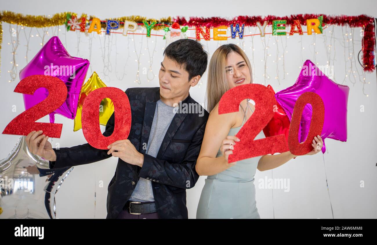 Gli amanti delle coppie asiatiche che tengono i numeri 2020 celebrando un nuovo anno in un bar gridando e ridendo e Contando fino a mezzanotte su una festa di nuovo anno Foto Stock