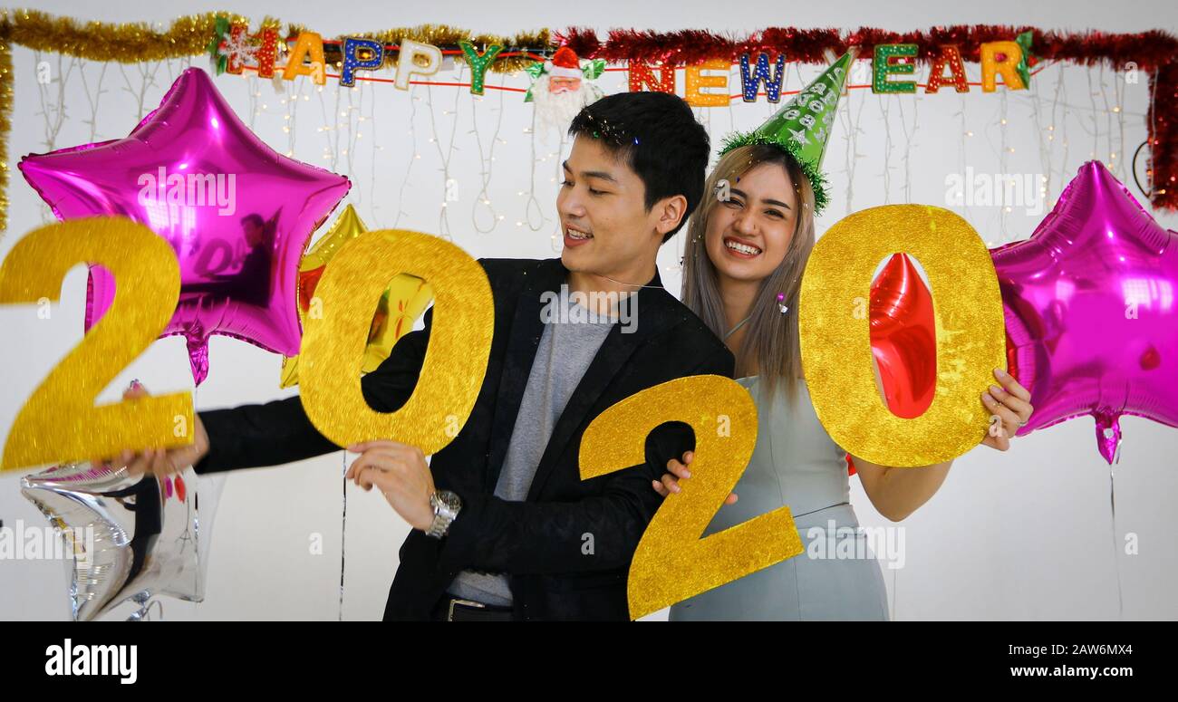Gli amanti delle coppie asiatiche che tengono i numeri 2020 celebrando un nuovo anno in un bar gridando e ridendo e Contando fino a mezzanotte su una festa di nuovo anno Foto Stock