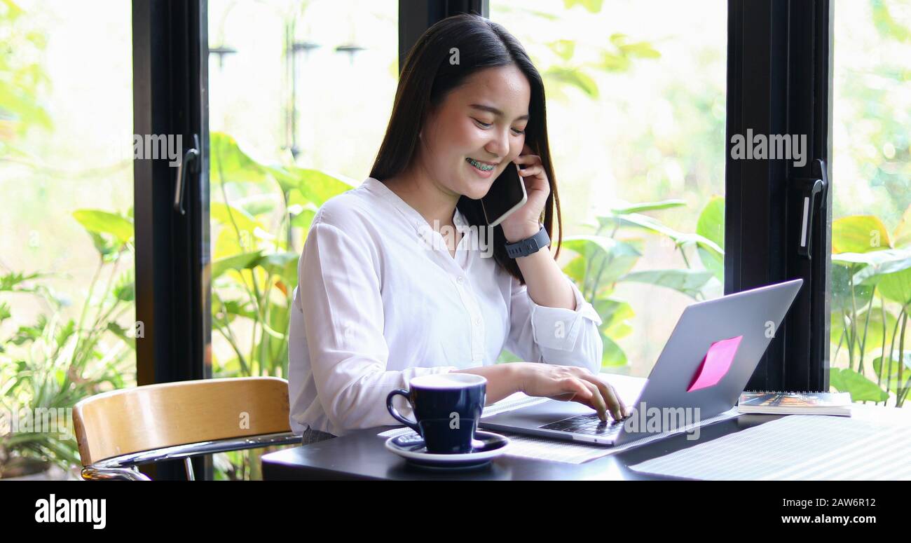 Le donne asiatiche di affari stanno usando lo smartphone mobile e del tocco per la comunicazione e le donne che usano il notebook per lavorare nella caffetteria Foto Stock