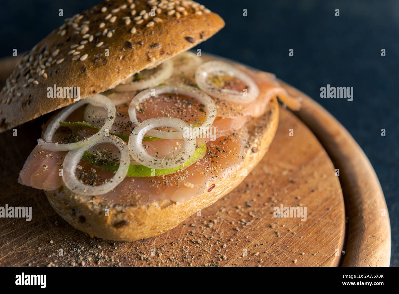 Vista ad alto angolo del panino a grano intero con salmone selvatico, anelli di cipolla e fette di pera su tavola di legno e tavolo scuro Foto Stock