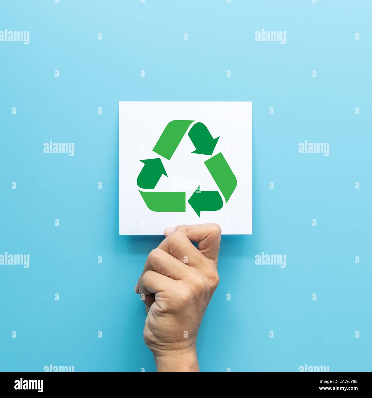 simbolo di riciclaggio verde su carta bianca in mano isolato su sfondo blu. concetto di business verde per azienda di consapevolezza ambientale Foto Stock