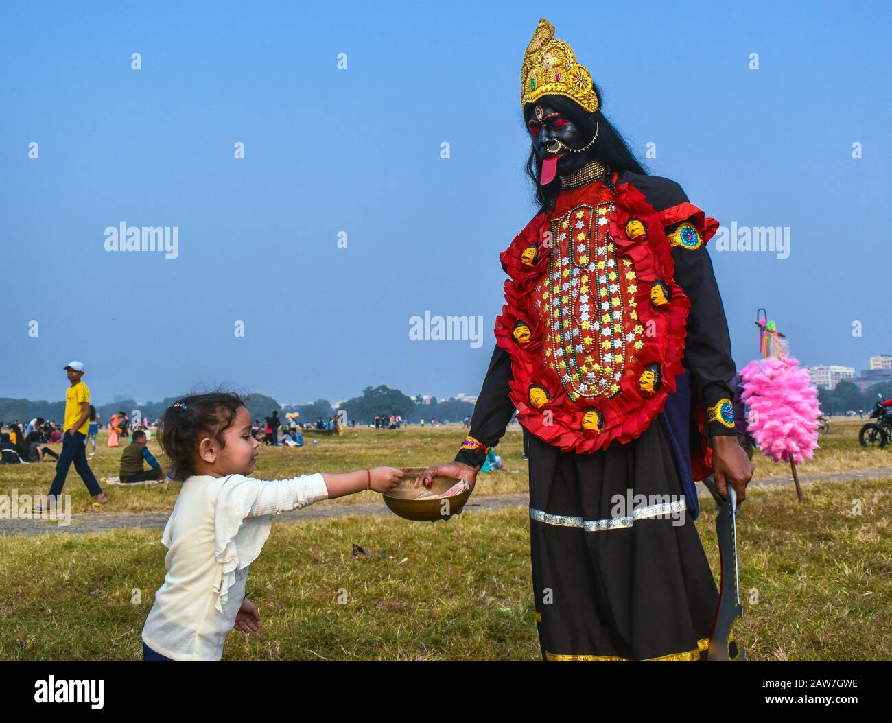 Una bambina sta dando denaro ad un Bohurupi, che si vestì come dea indù ma Kali a Kolkata, India. Foto Stock