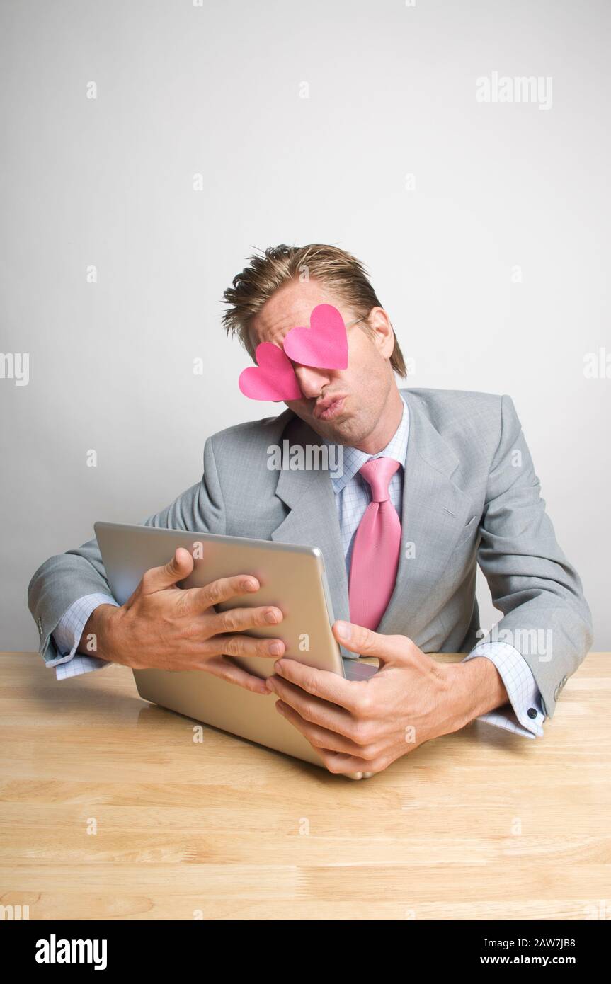 Lavoratore di ufficio accecati da cuori rosa raggrinzamenti fino ad un bacio abbracciando il computer portatile sulla sua scrivania Foto Stock
