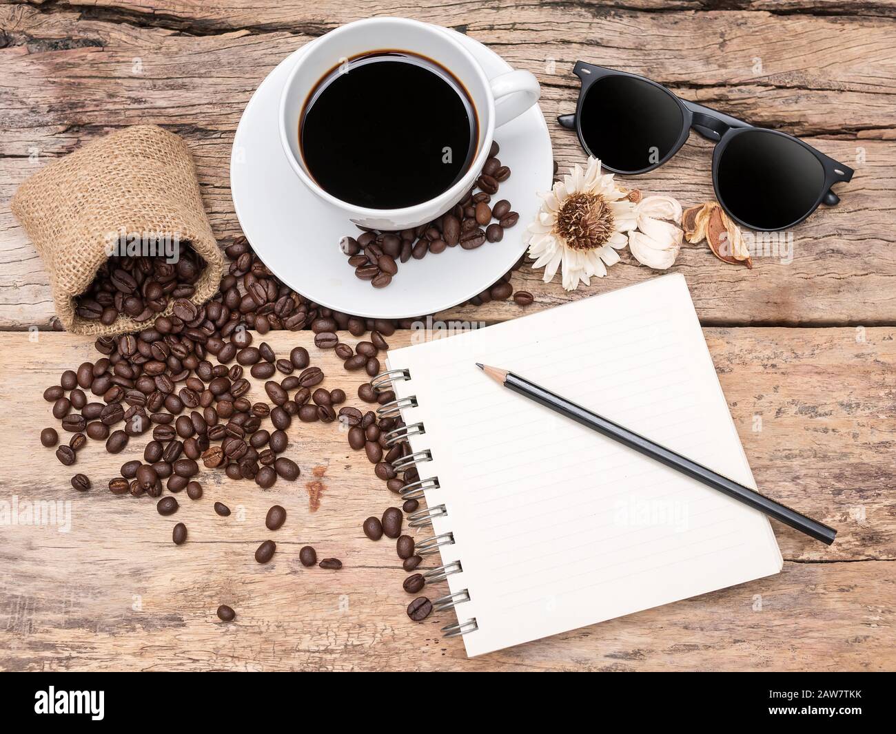 caffè espresso fresco con chicchi di caffè su tavola di legno decorare con fiori secchi, occhiali da sole e vuoto pagina libro bianco. caffè sfondo menu f Foto Stock