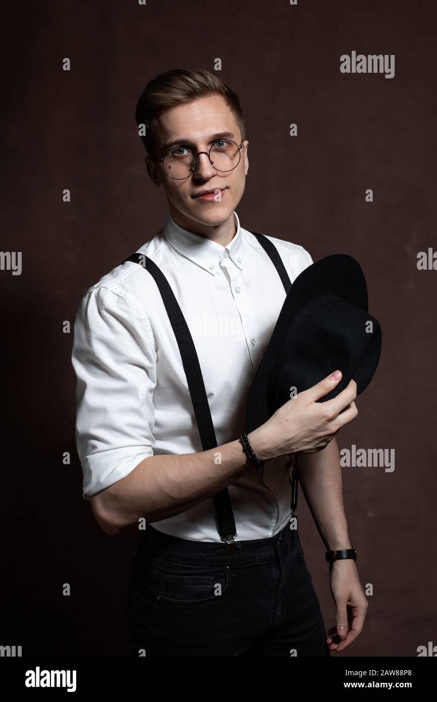 Giovane uomo con occhiali rotondi, bretelle, camicia bianca e cappello su  sfondo marrone Foto stock - Alamy