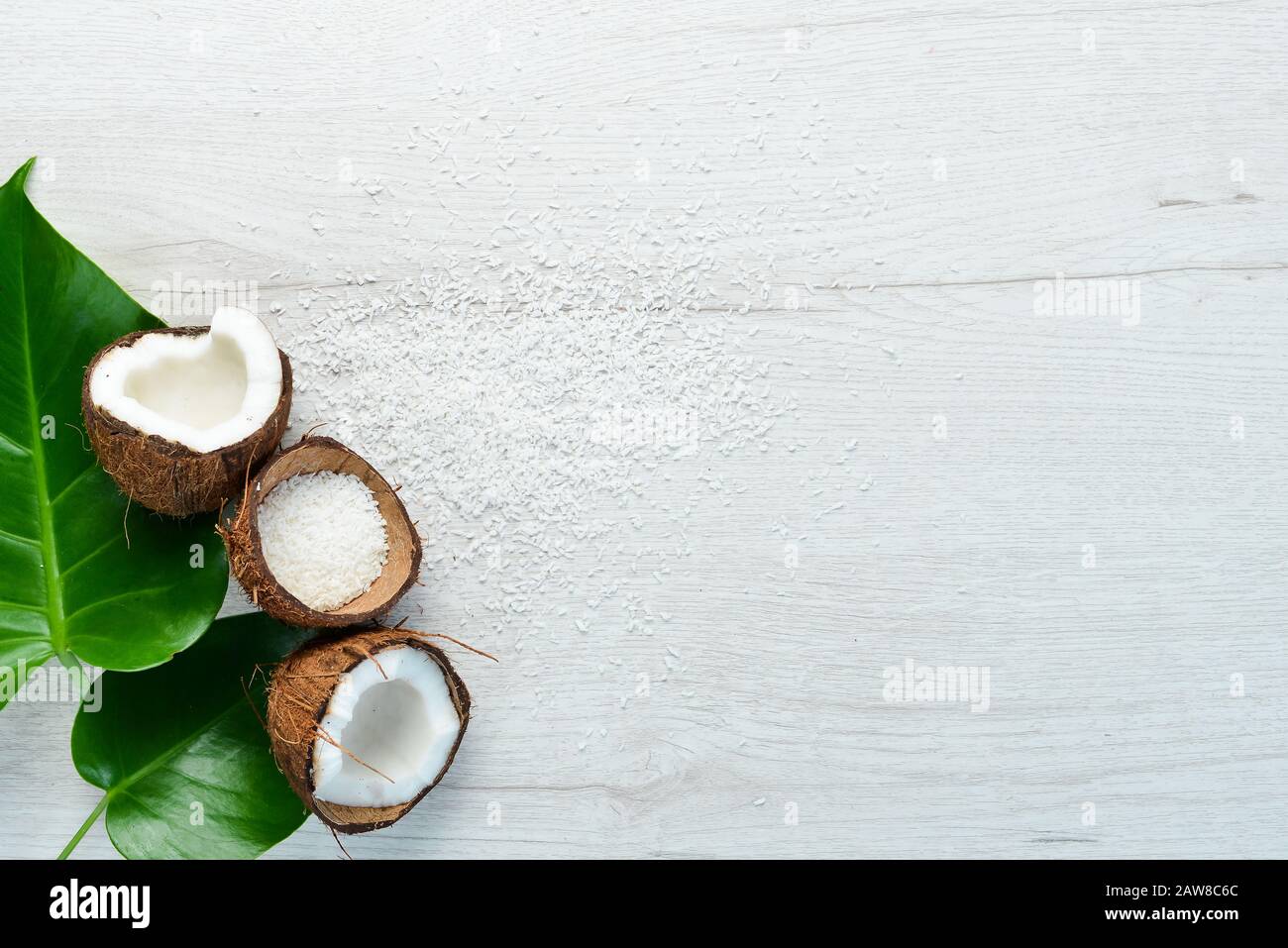 Cosmetici a base di cocco e foglie tropicali. Su uno sfondo di legno bianco. Disposizione piatta. Foto Stock