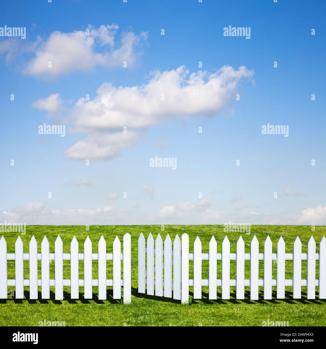 Una recinzione bianca in picchetto e porta aperta che conduce ad un bel campo verde e cielo blu in estate Foto Stock