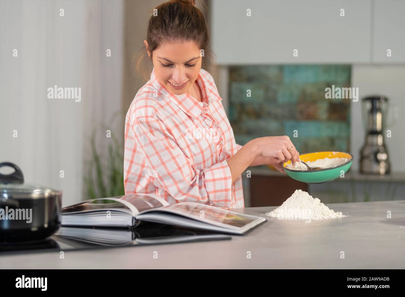 Donna che tiene una ciotola e che controlla un libro di cucina Foto Stock