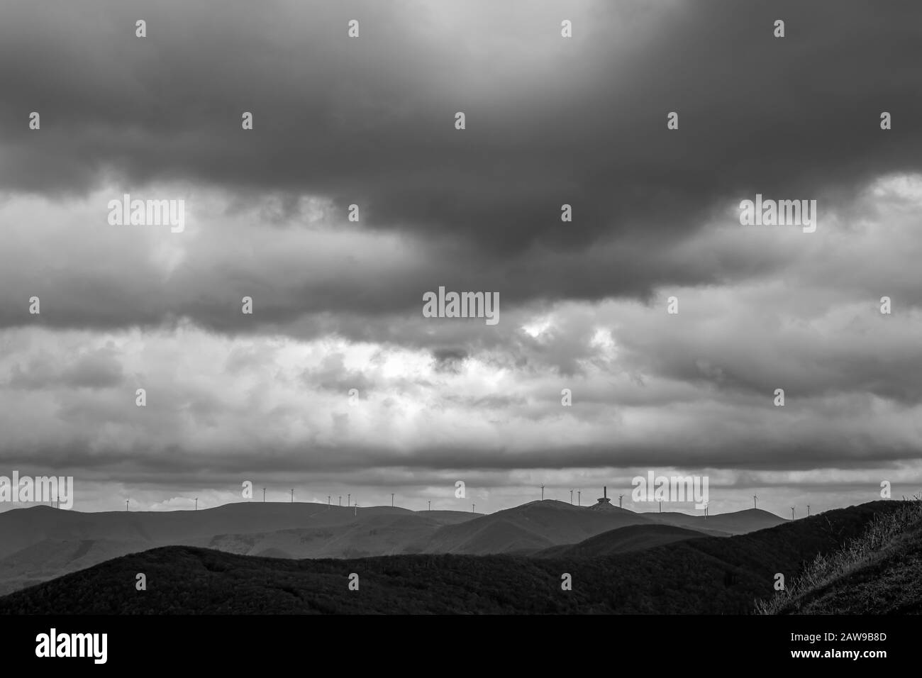 Spettacolare vista in bianco e nero autunnale del congresso comunista in rovina edificio sulla vetta di Buzludzha, Stara Planina montagna nella Bulgaria centrale, visto dal memoriale Shipka. Diverse turbine eoliche Foto Stock