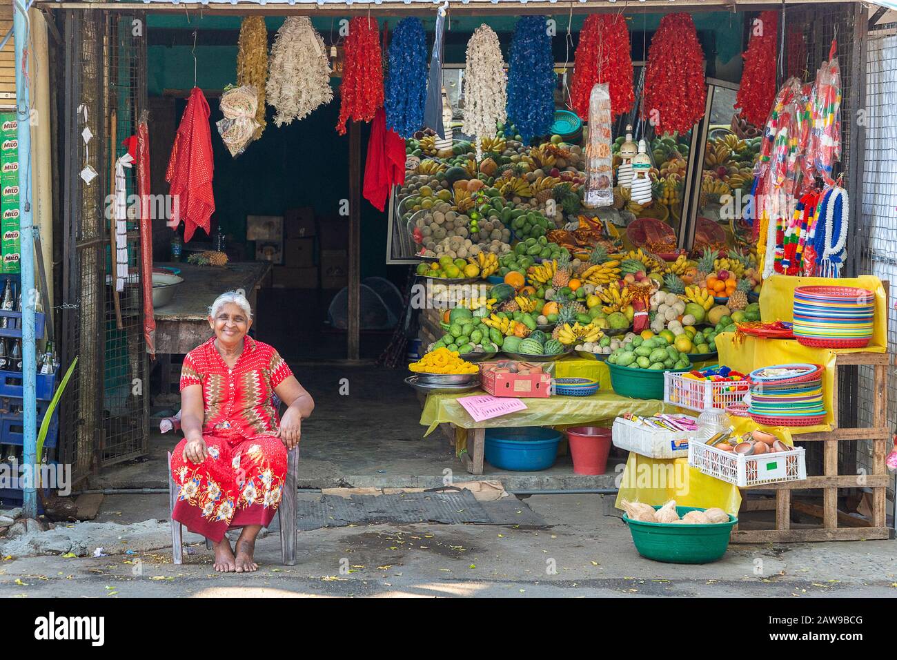 Donna locale seduto di fronte al suo negozio di alimentari, a Kataragama, Sri Lanka Foto Stock