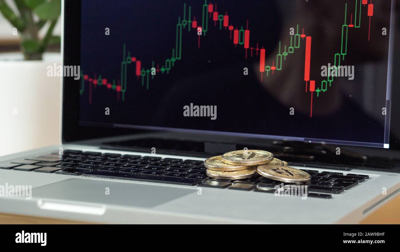 Monete Bitcoin su un laptop con grafico dei prezzi in background Foto Stock