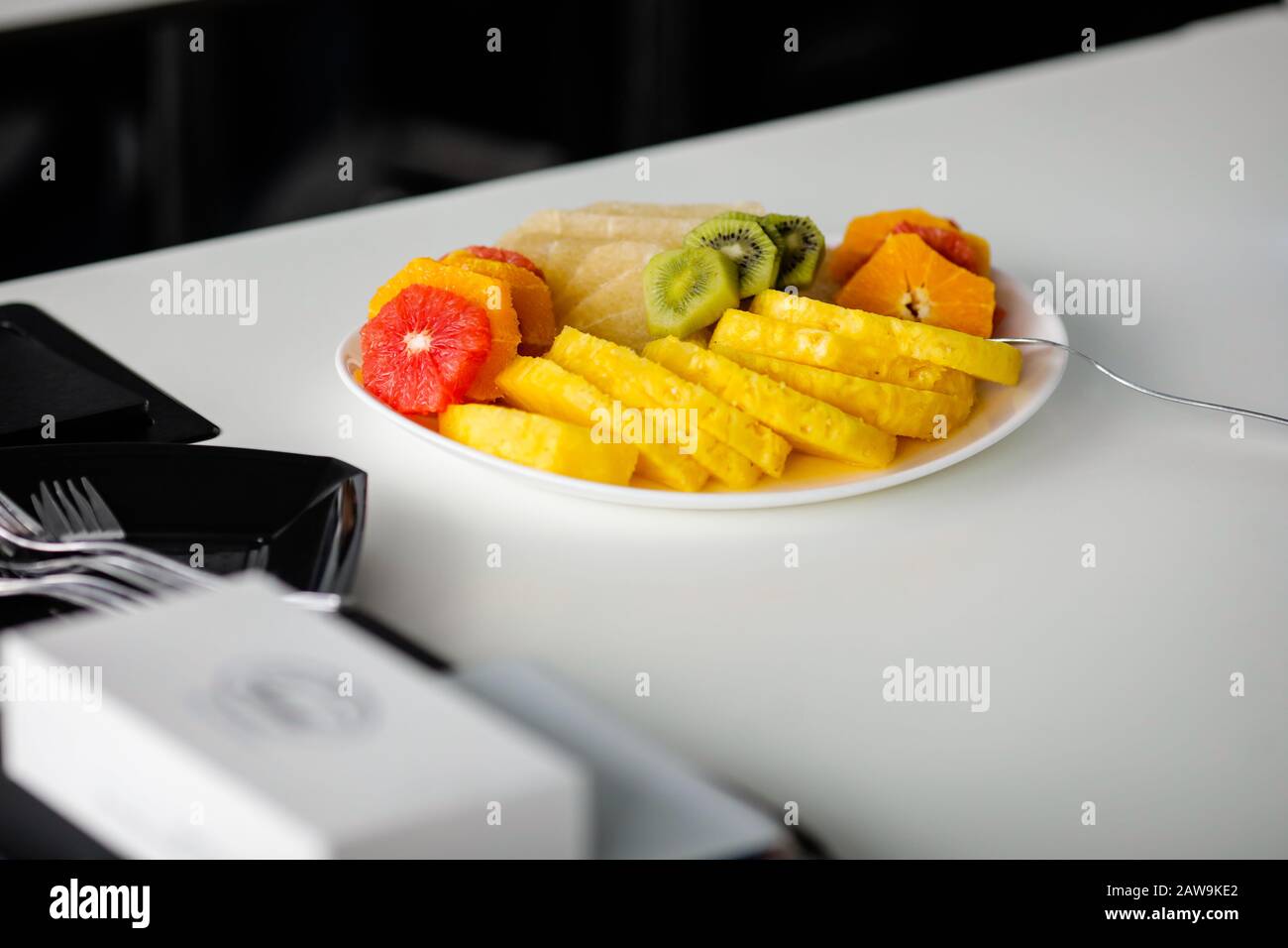 Immagine con profondità di campo bassa (fuoco selettivo) con vari frutti tagliati in pezzi su una piastra su un tavolo bianco. Foto Stock