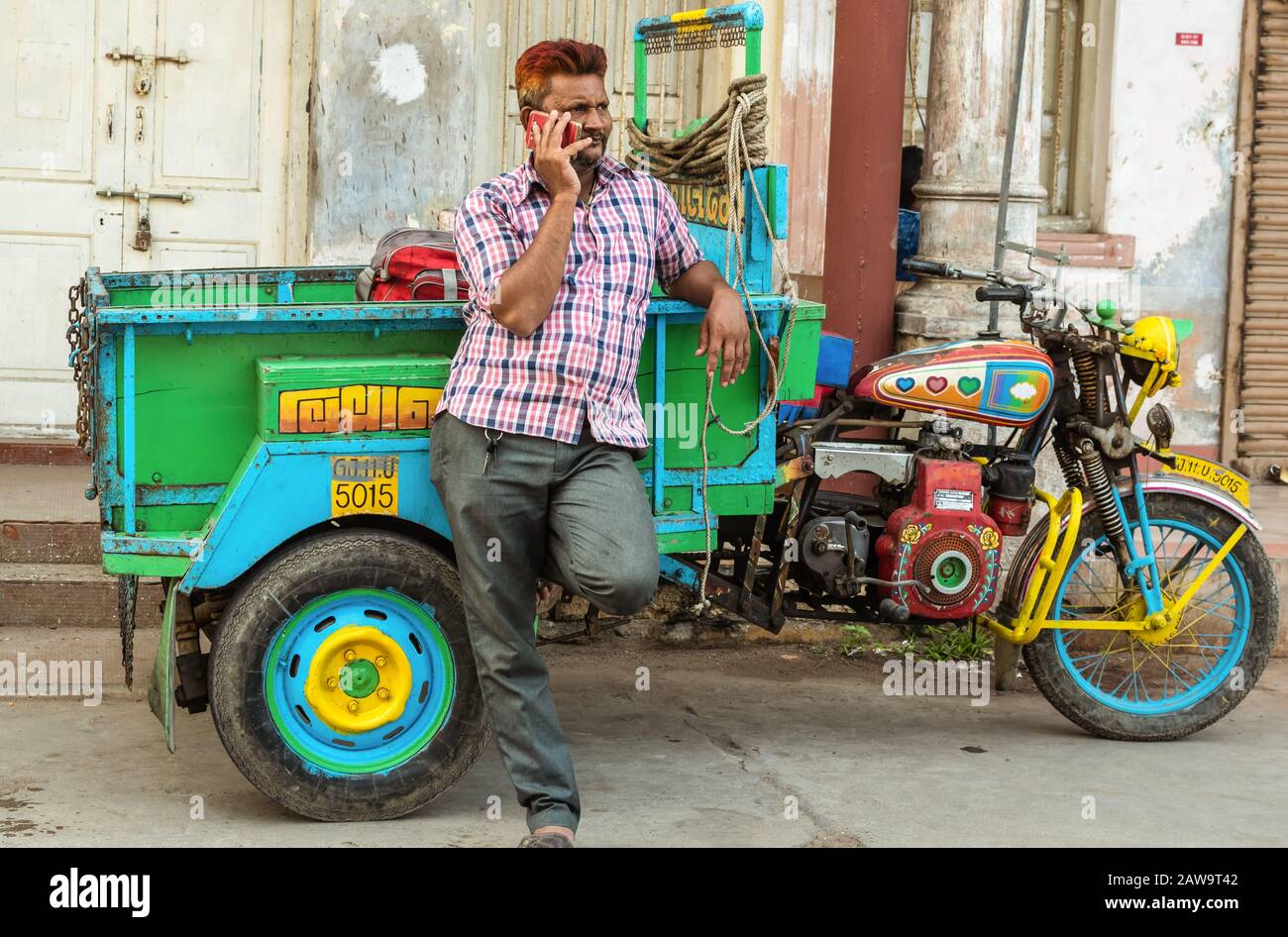 Diu, India - dicembre 2018: Un ritratto di un pilota di risciò che si trova accanto al suo risciò colorato e parla sul suo cellulare. Foto Stock