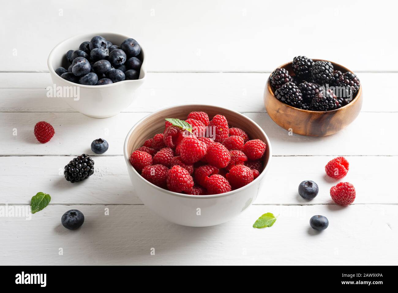 tre ciotole con frutti di bosco, lampone, mirtilli, more, su sfondo di legno bianco Foto Stock