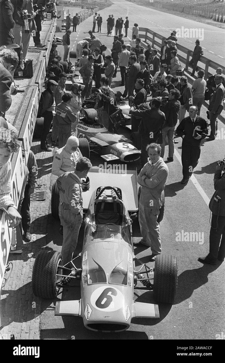 Nederlands: No. 6 in de drukke pitstraat. Bruce McLaren (al centro a sinistra, balaclava bianca) si prepara a prendere il suo posto nella sua McLaren M7C di Formula Uno, prima del Gran Premio d'Olanda del 1969. Dietro, il driver francese Jean-Pierre Beltoise (casco su) sta per salire a bordo della sua Matra MS80.; Foto Stock