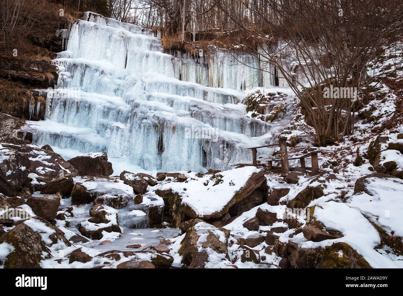 Bella, panoramica, ghiacciata cascata di Tupavica con ghiaccioli appesi e torrente di montagna ghiacciato con rocce arancioni Foto Stock