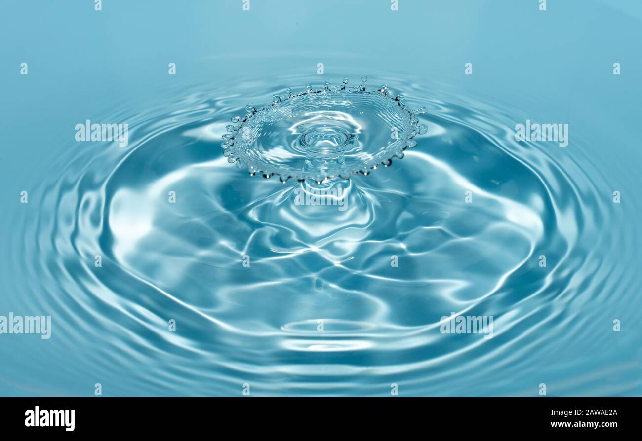 Gocce di acqua pulita e fresca cadono da un'altezza di acqua blu trasparente che forma schizzi sotto forma di figure originali. Foto Stock
