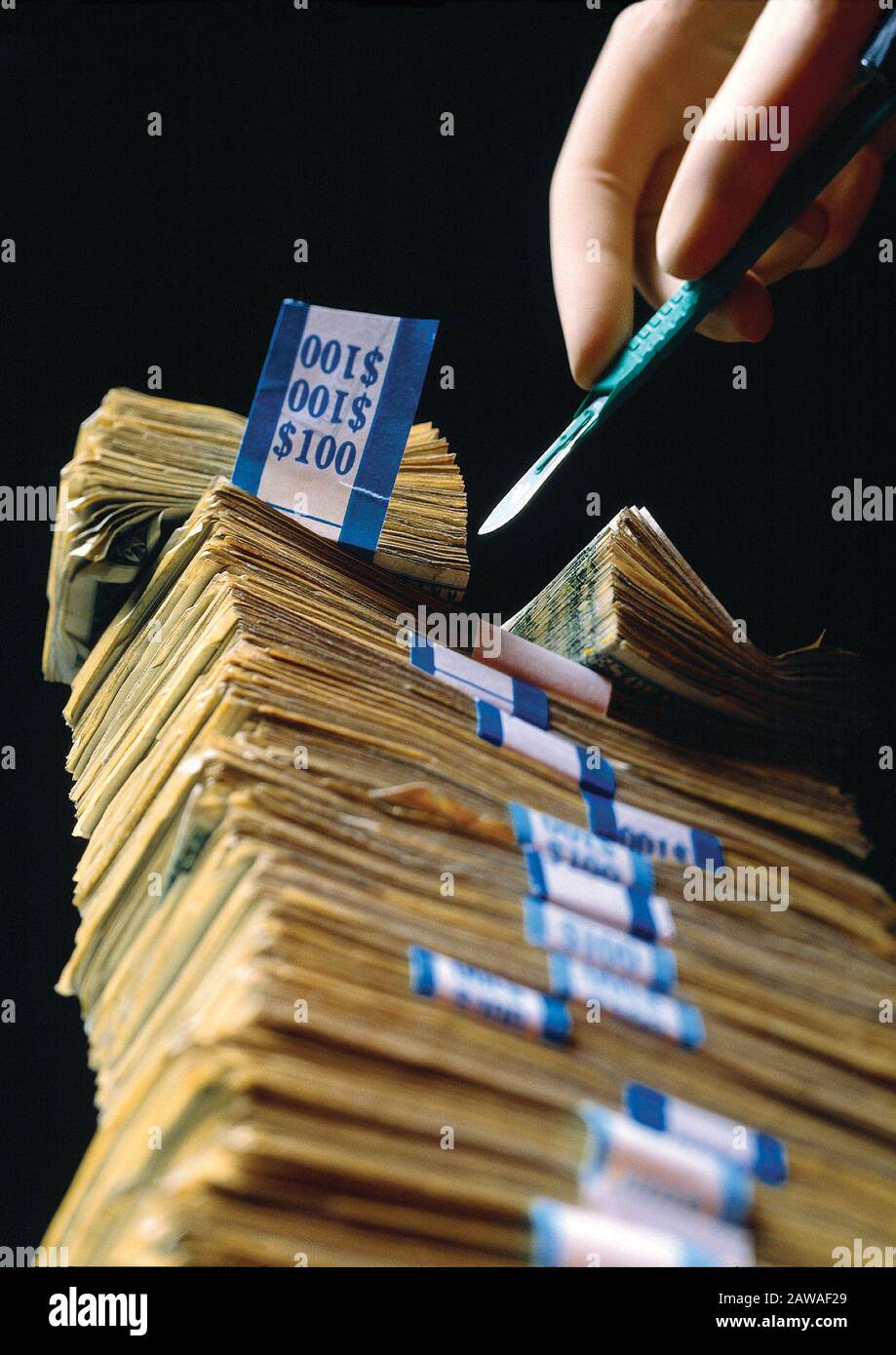 Una mano dei chirurghi che tiene un bisturi che taglia attraverso una pila di banconote da cento dollari che illustra l'alto costo dell'assistenza medica Foto Stock
