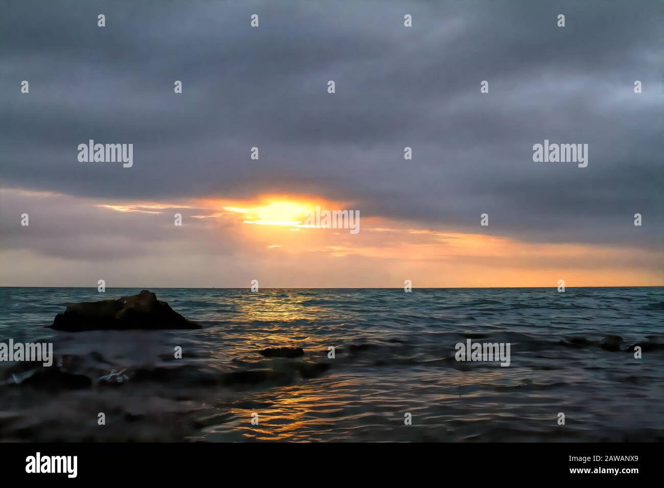 La bellezza della natura: Un'alba scura minacciosa in una giornata torbida che si affaccia sull'oceano con un riflesso sull'acqua. Foto Stock