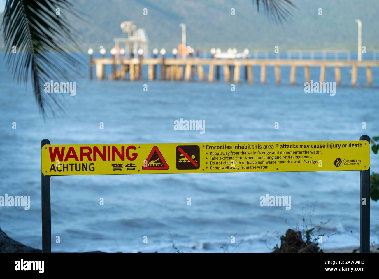 Segnale di avvertimento coccodrillo sulla spiaggia di Cardwell con Jetty sullo sfondo. Cardwell North Queensland, Australia Foto Stock