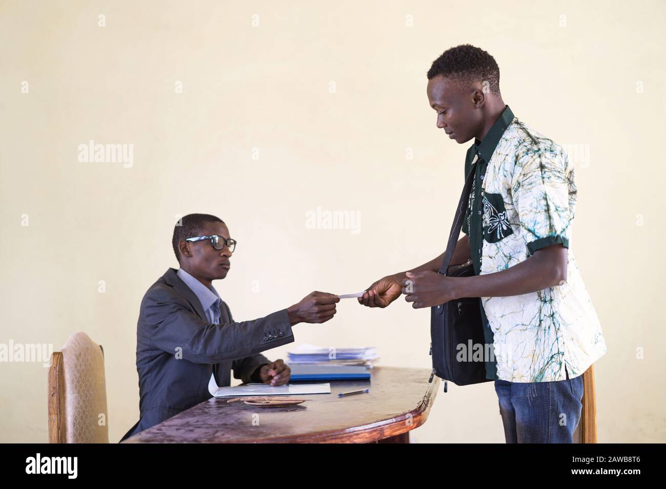 Un uomo d'affari africano di successo e uno studente che consegna la sua carta d'identità per identificare la sua azienda in un ufficio Foto Stock