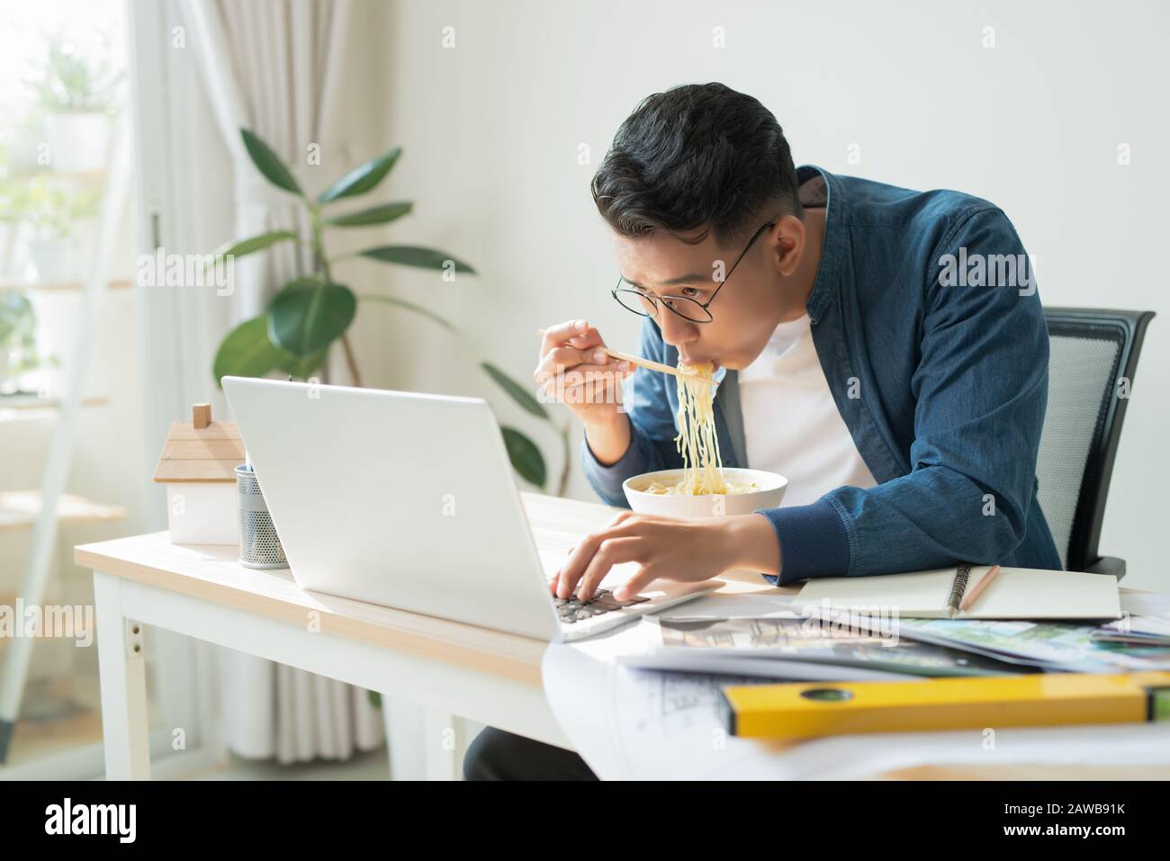 Allegro ingegnere con dessert seduto di fronte al monitor del computer e mangiare noodle Foto Stock