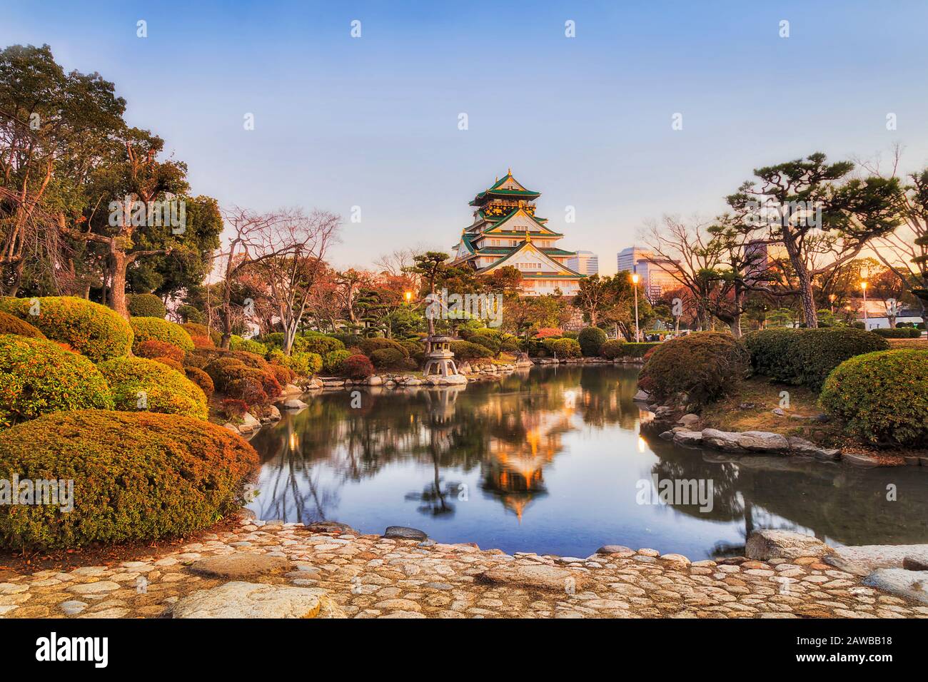 Piccolo stagno ancora nel mezzo del parco pubblico e della zona storica della città di Osaka all'alba. Riflessione di pini verdi e torre del castello patrimonio. Foto Stock