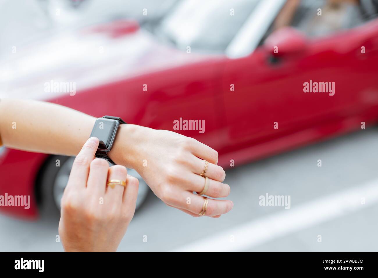 Donna con smartwatch al parcheggio con veicolo rosso sullo sfondo, vista ravvicinata sull'orologio con schermo nero. Controllo dell'auto con un concetto di orologio intelligente Foto Stock