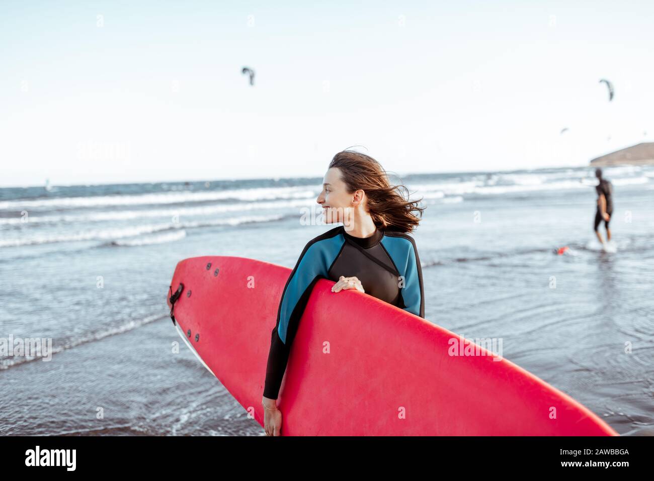 Ritratto di una giovane donna surfista in costume da bagno in piedi con tavola da surf rossa sulla spiaggia. Stile di vita attivo e concetto di surf Foto Stock