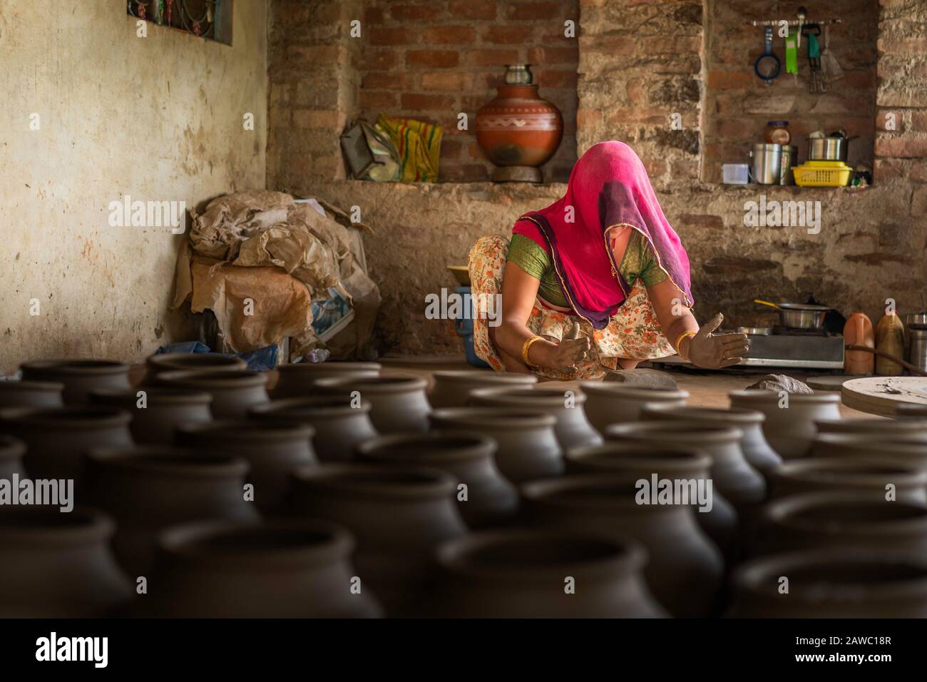 Donna in abiti tradizionali colorati inginocchia argilla umida in preparazione per il vasaio nel villaggio di Bundi, Rajasthan, India. Foto Stock