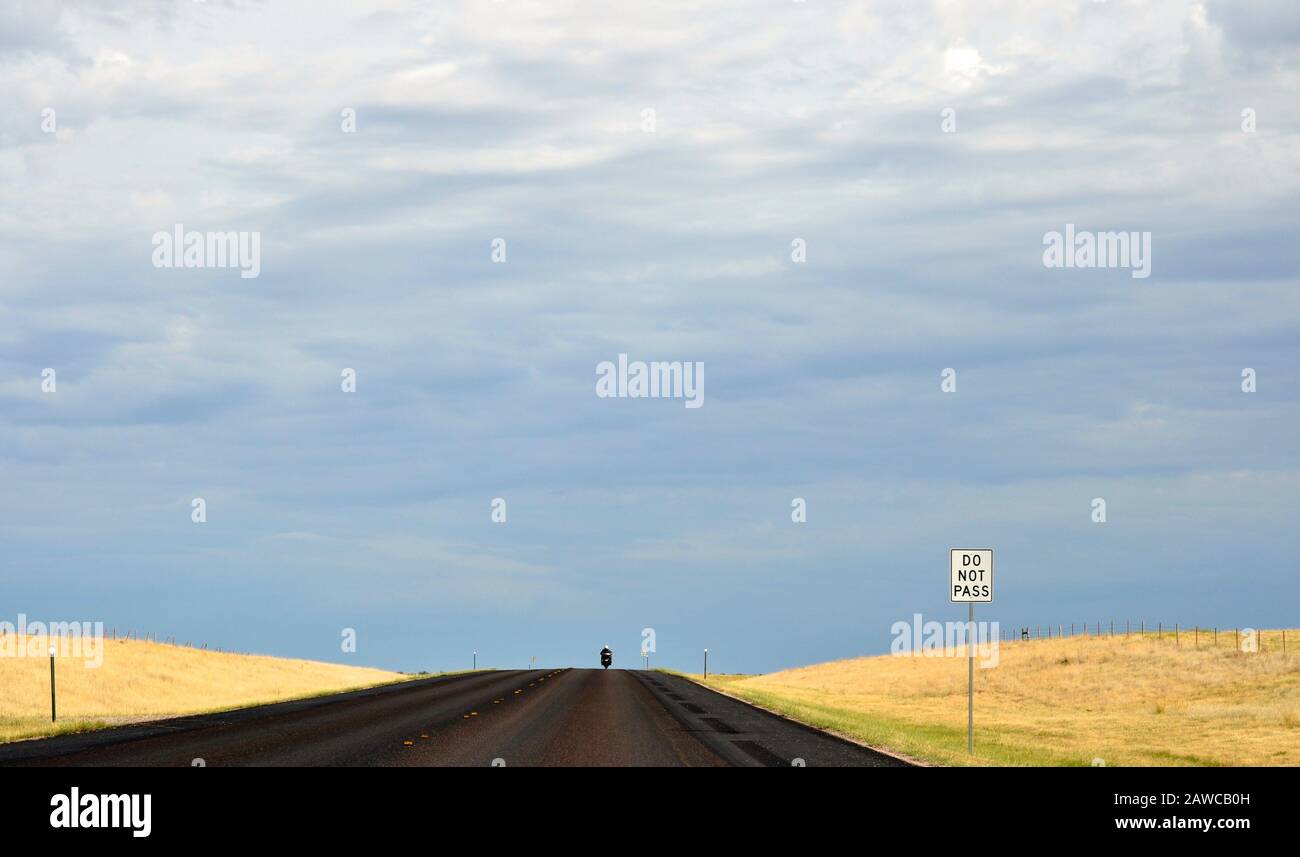 Un motociclista solitario fa un giro in moto su un'autostrada vuota attraverso i campi gialli verso una tempesta estiva - South Dakota, USA Foto Stock