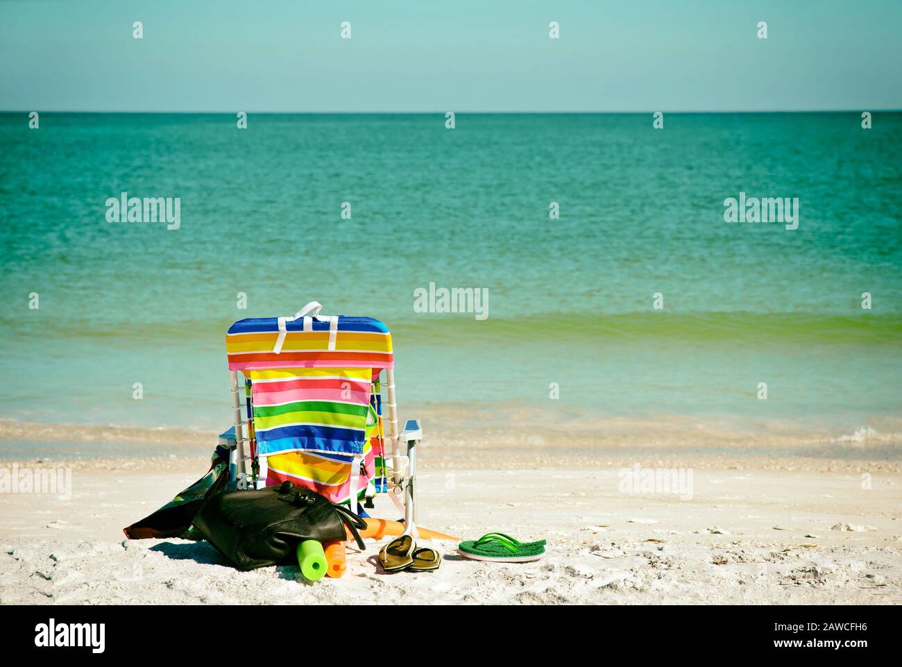 Luminosa sedia da spiaggia a colori con infradito, galleggianti e borsa sulla spiaggia Foto Stock