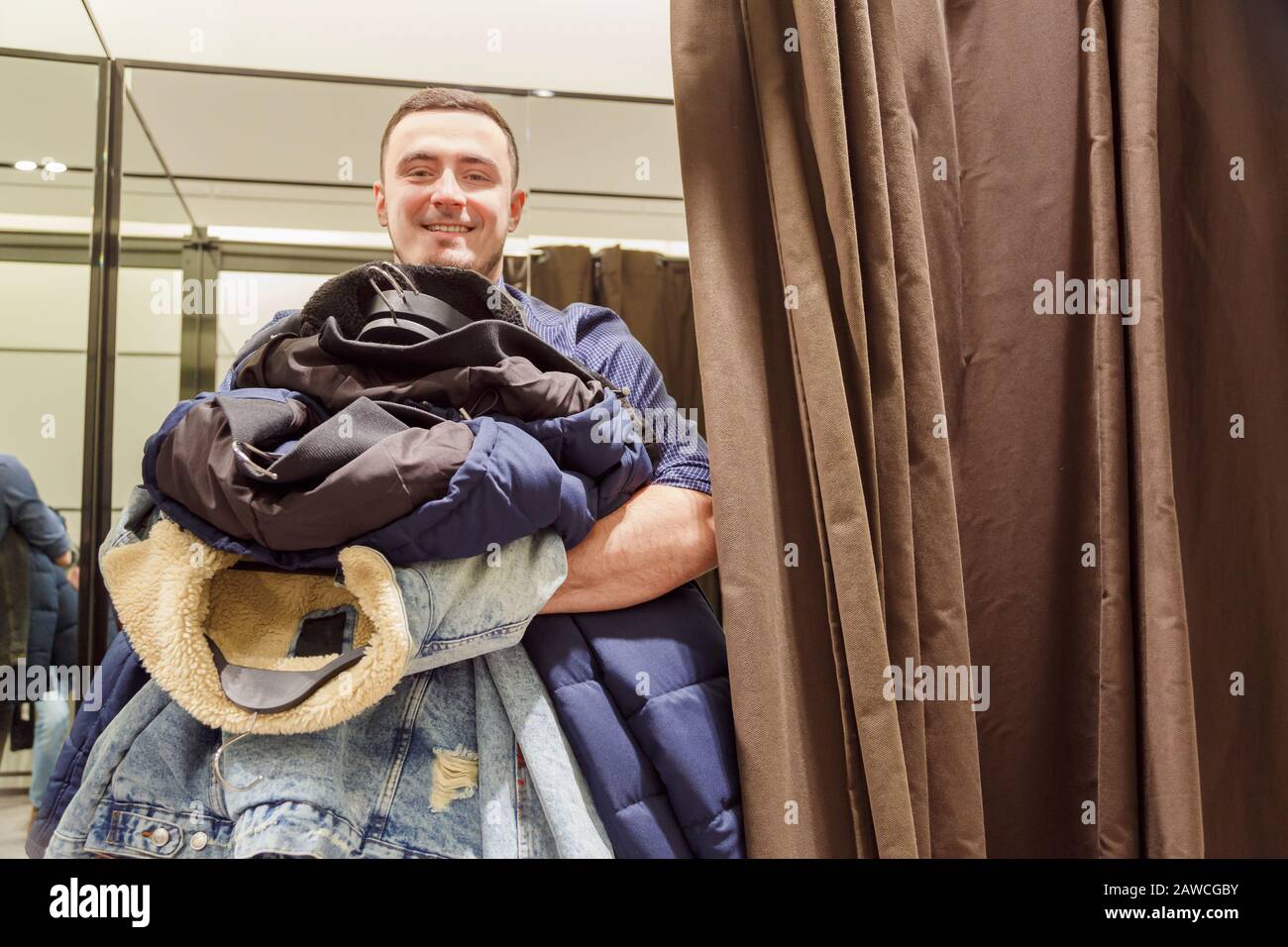 Giovane uomo con un armful di vestiti nella stanza di montaggio durante la  vendita e sconti Foto stock - Alamy