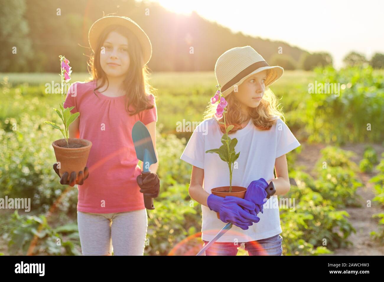 Ritratto di due bambini con fiori in vaso, guanti, con pale da giardino Foto Stock