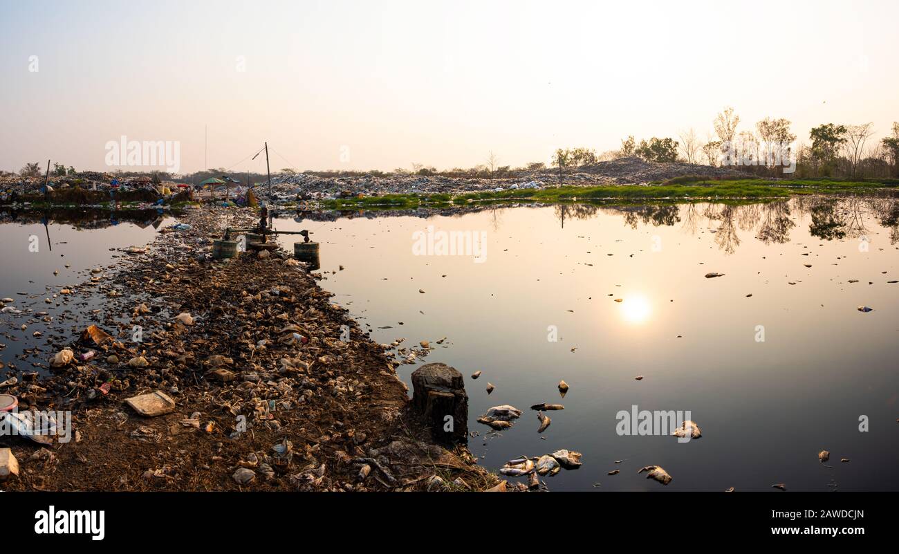 Acqua inquinata e montagna grandi rifiuti pile e l'inquinamento al sole sta tramontando in background, pile di stink e residui tossici, Questi rifiuti com Foto Stock