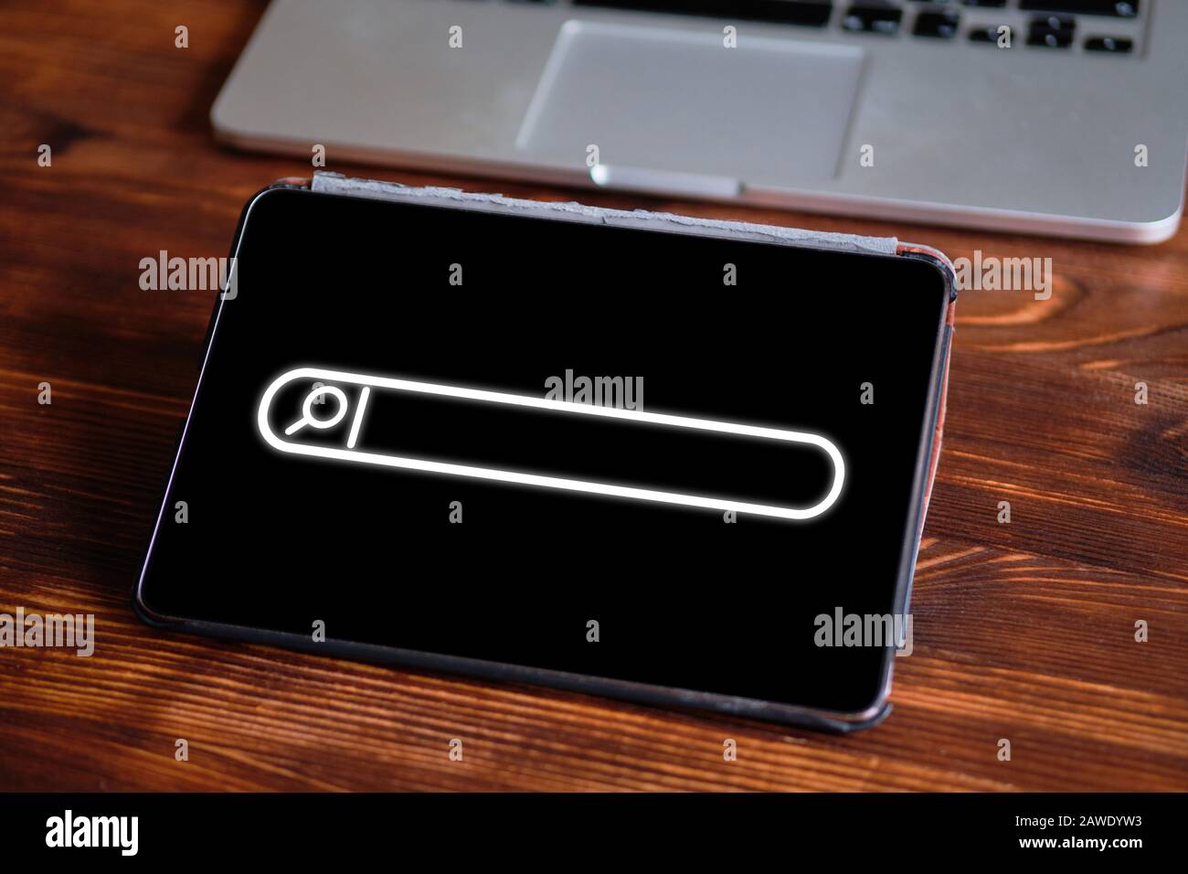 Cerca la linea con una lente di ingrandimento su un tablet accanto a un notebook su un tavolo di legno. Il concetto di ricerca di informazioni su Internet. Primo piano Foto Stock