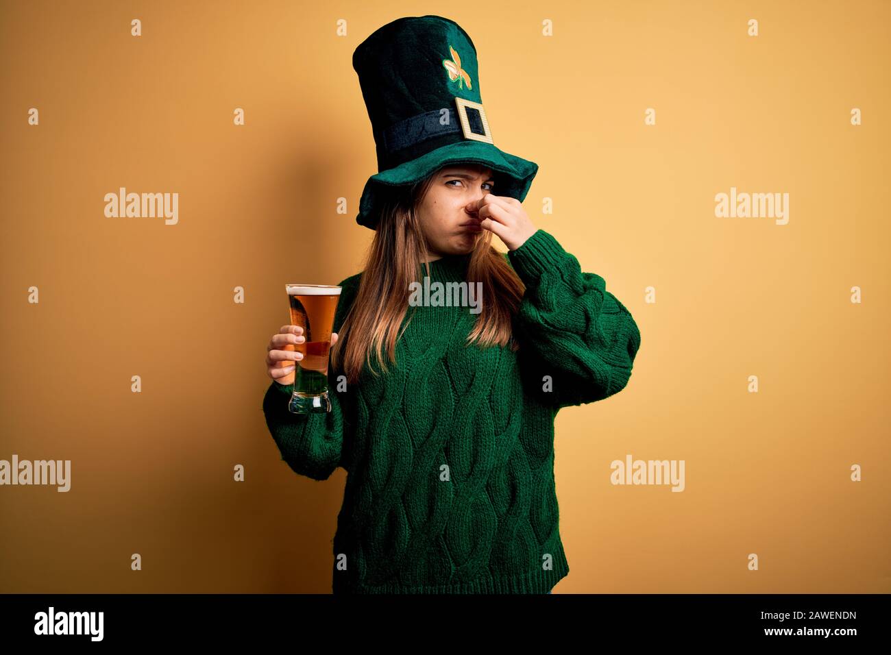 Giovane bella donna che indossa cappello verde bere un bicchiere di birra su san patricks giorno odorare qualcosa di puzzolente e disgustoso, odore intollerabile, tenere Foto Stock