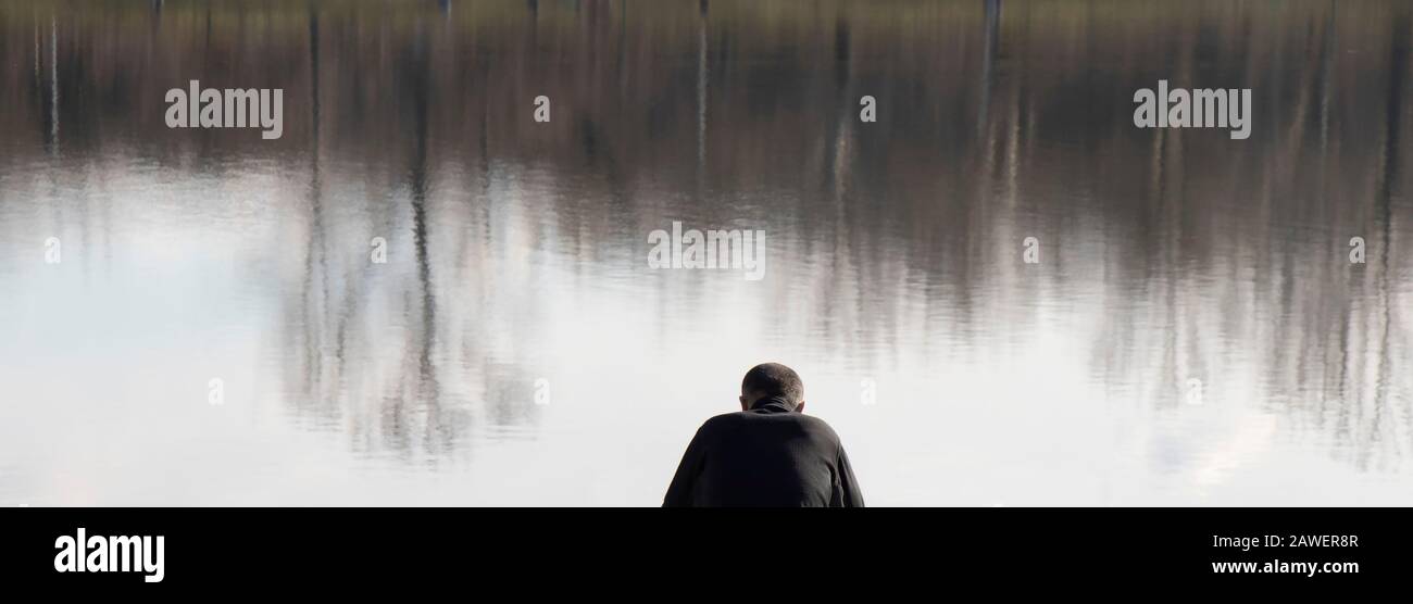 Belgrado, Serbia - 2 febbraio 2020: Un uomo in nero seduto da solo su una riva del lago, con riflessi sull'acqua Foto Stock
